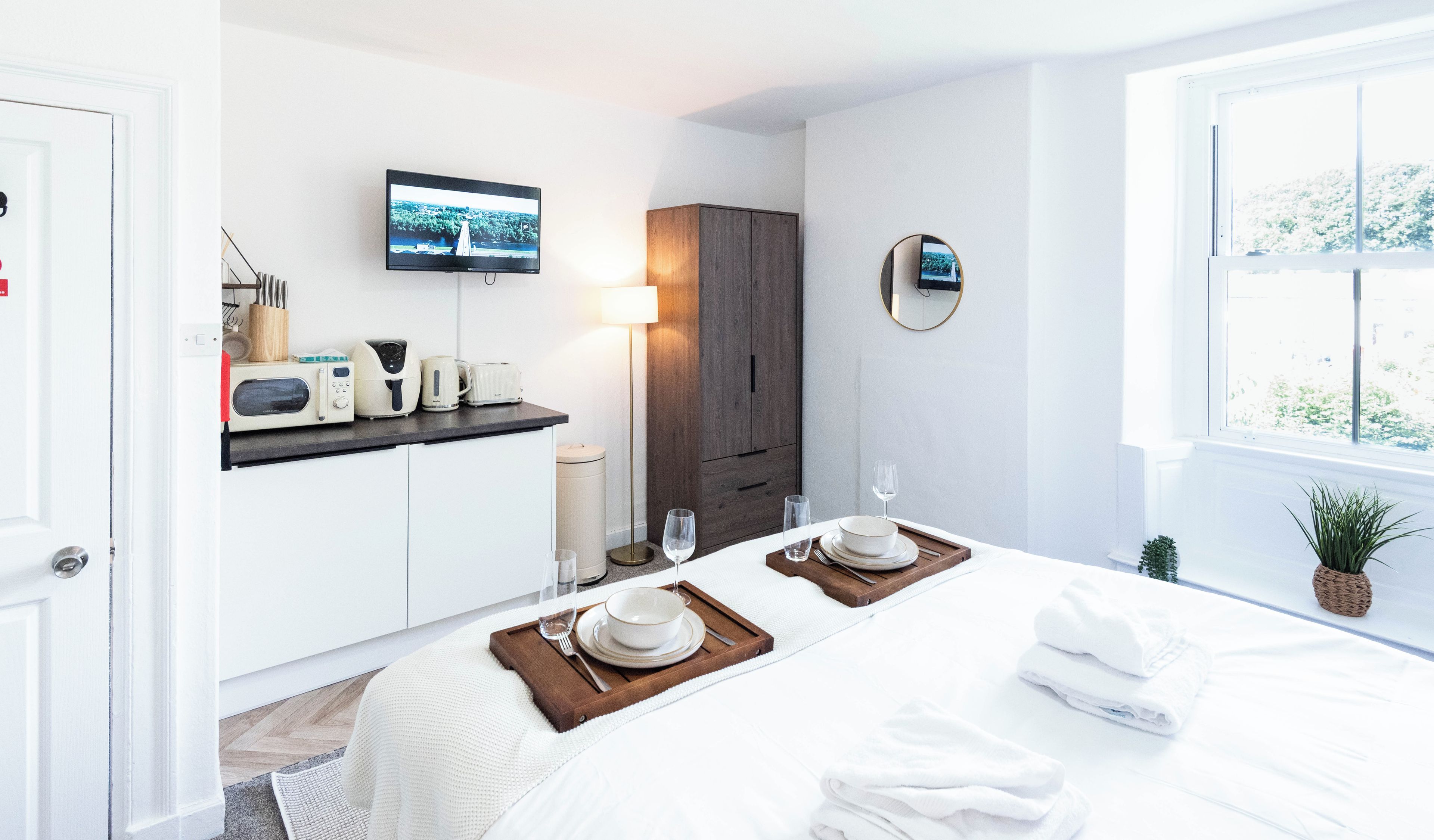 A hotel room with a bed, a TV, a wooden cabinet, a mirror, and a window with a view.