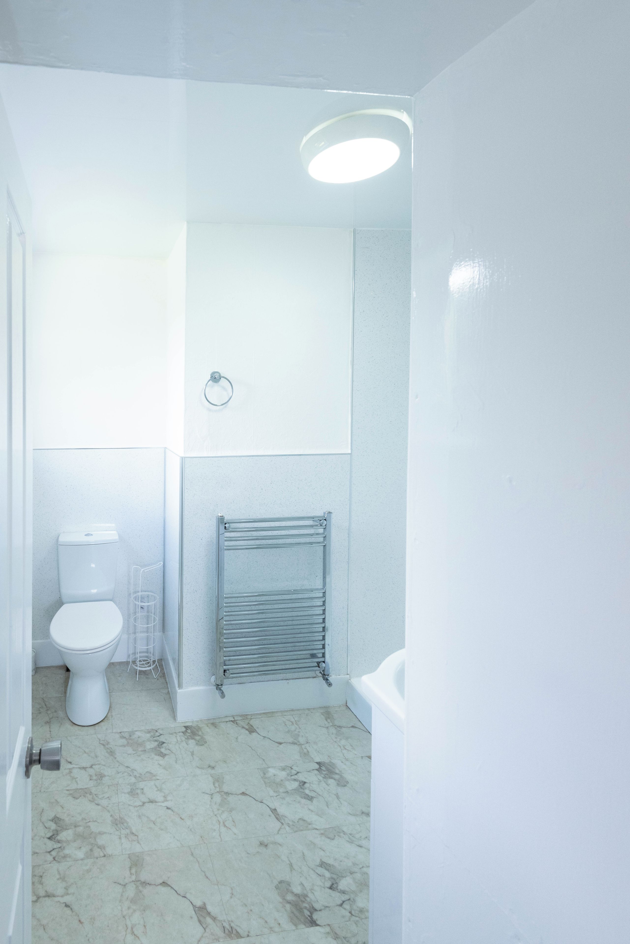 A bathroom with a toilet, a towel rack, a radiator, and a marble floor.