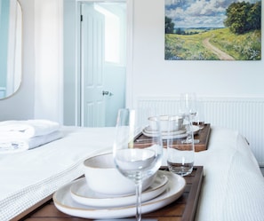 A neatly arranged dining table with white plates, bowls, and glasses, set against a white wall with a landscape painting. - The Stanley Arms Hotel by Guestz (Seascale)