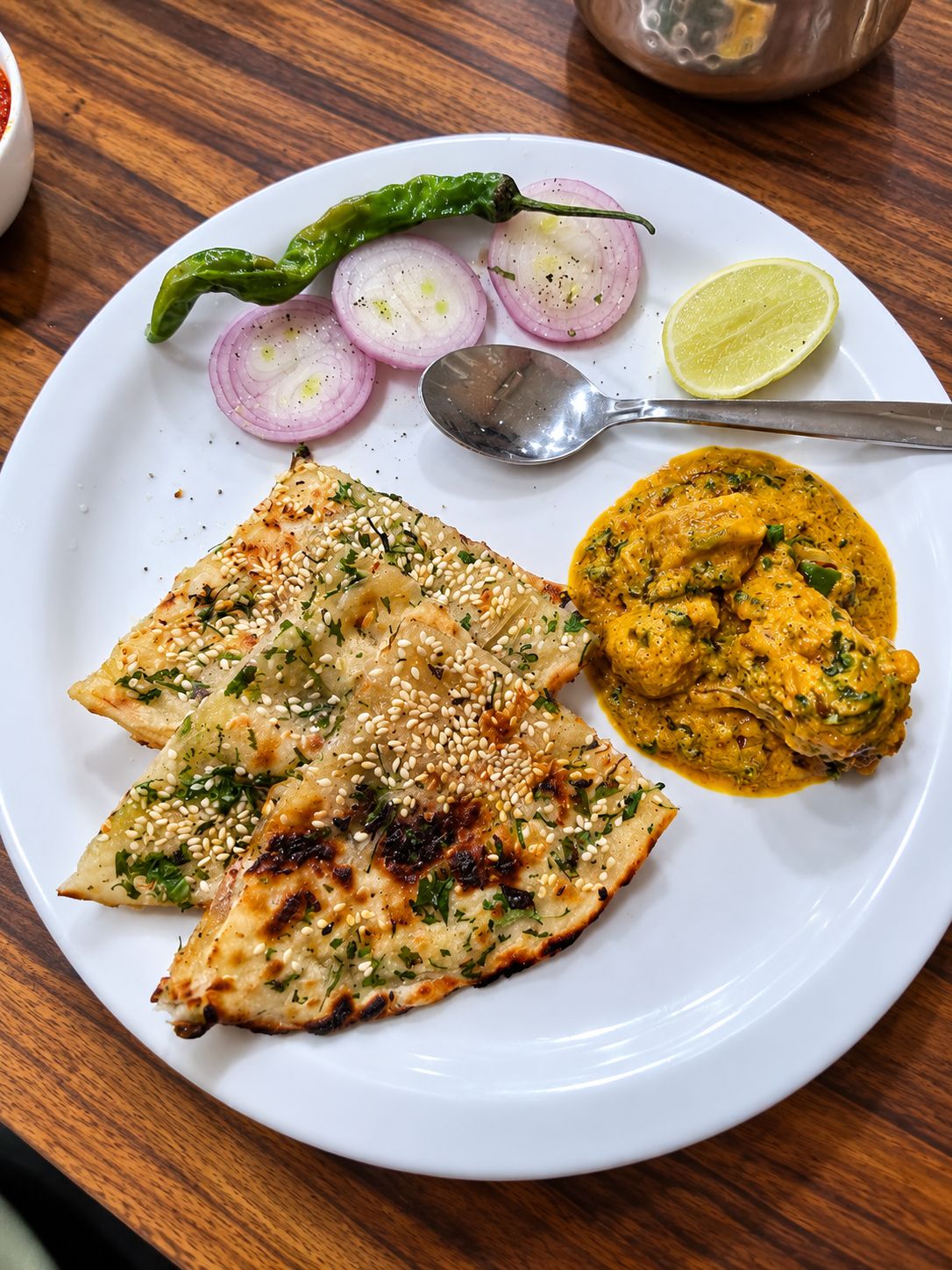 A plate with flatbread, sliced onions, a green chili, a lime wedge, and a spoon.
