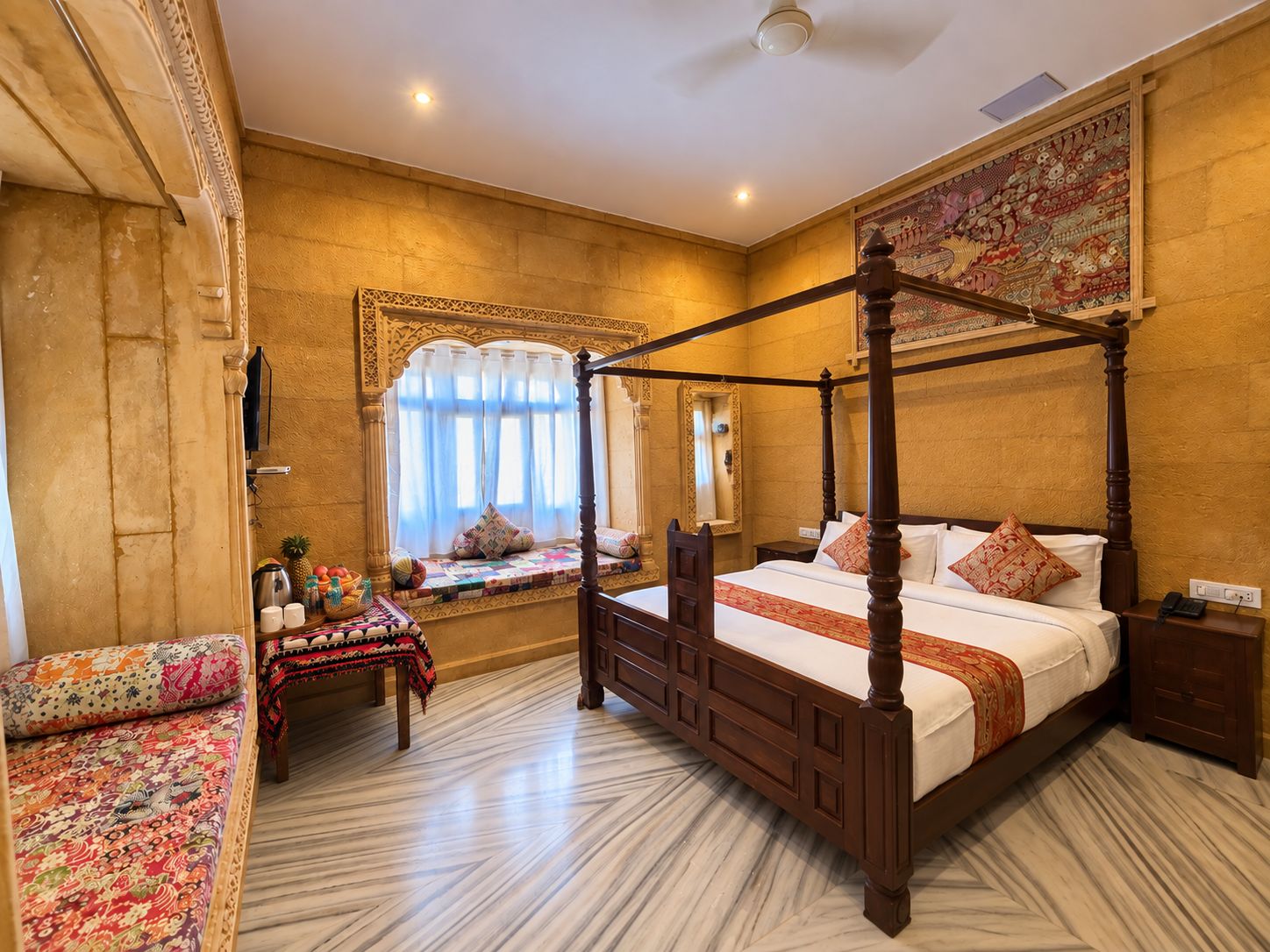A four-poster bed with a canopy, a bench with a patterned cushion, a small table with a decorative cloth, and a large tapestry on the wall.