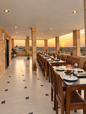 A rooftop dining area with tables and chairs, potted plants, and a view of the city skyline at sunset. - HOTEL ROYAL LAKHINA JAISALMER (Jaisalmer)