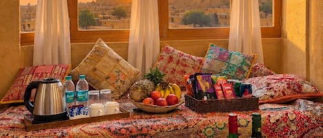 A room with a bed, a tray with drinks and snacks, and a view of a cityscape at sunset.