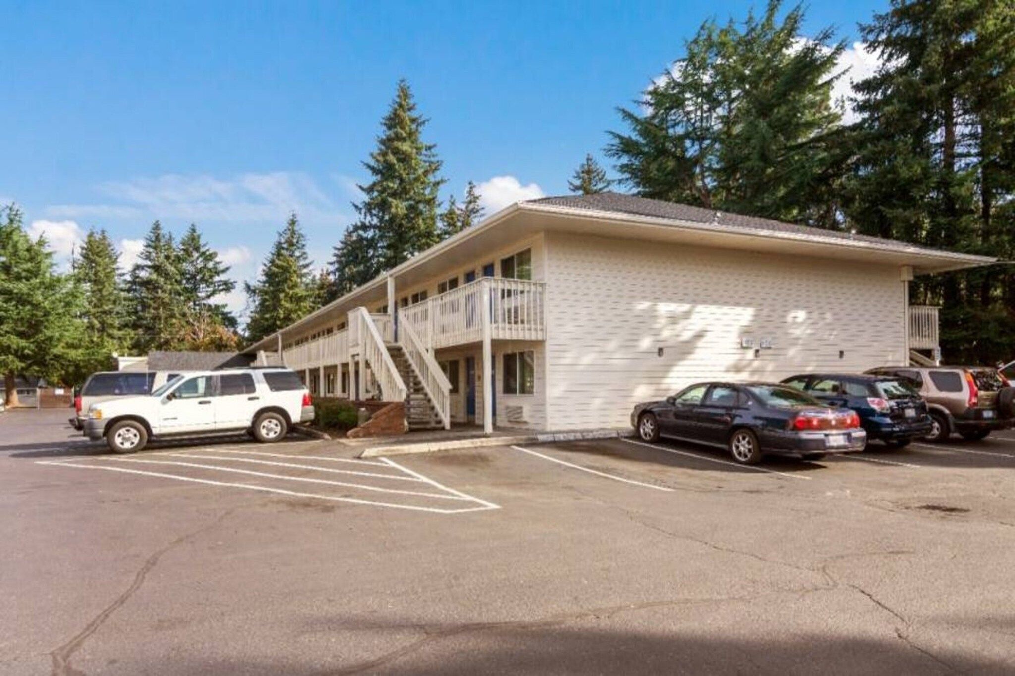 Un motel composé d’un bâtiment à deux étages, d’un espace extérieur abrité et d’un parking où sont stationnés plusieurs véhicules.