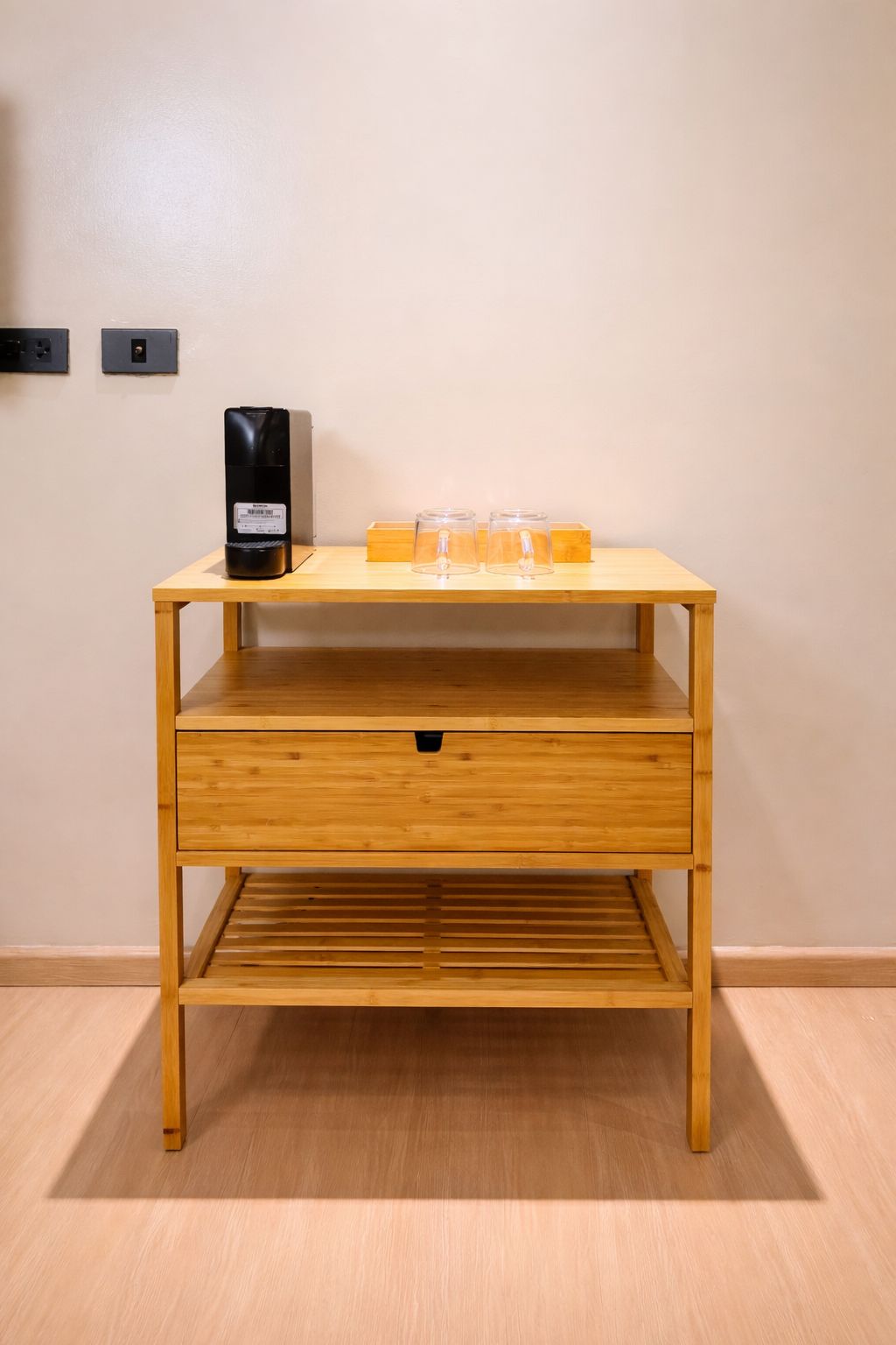 Ein Nachttisch aus Holz mit einer Schublade, ein schwarzes elektronisches Gerät und zwei klare Glasbehälter darauf.