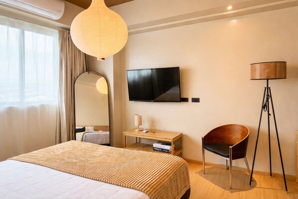 A hotel room with a large bed, a flat-screen TV, a bedside table with a lamp, a floor lamp, and a mirror.