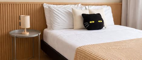 A hotel room with a bed, a bedside table with a lamp, and a black cat-shaped pillow.