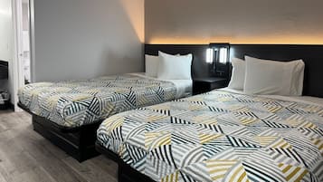 A hotel room with two beds, each with patterned bedding, a bedside table with a lamp, and a wall-mounted light fixture.