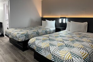 Ein Hotelzimmer mit zwei Betten, jeweils mit gemusterten Bettbezügen, einem Nachttisch mit Lampe sowie einer Wandleuchte.