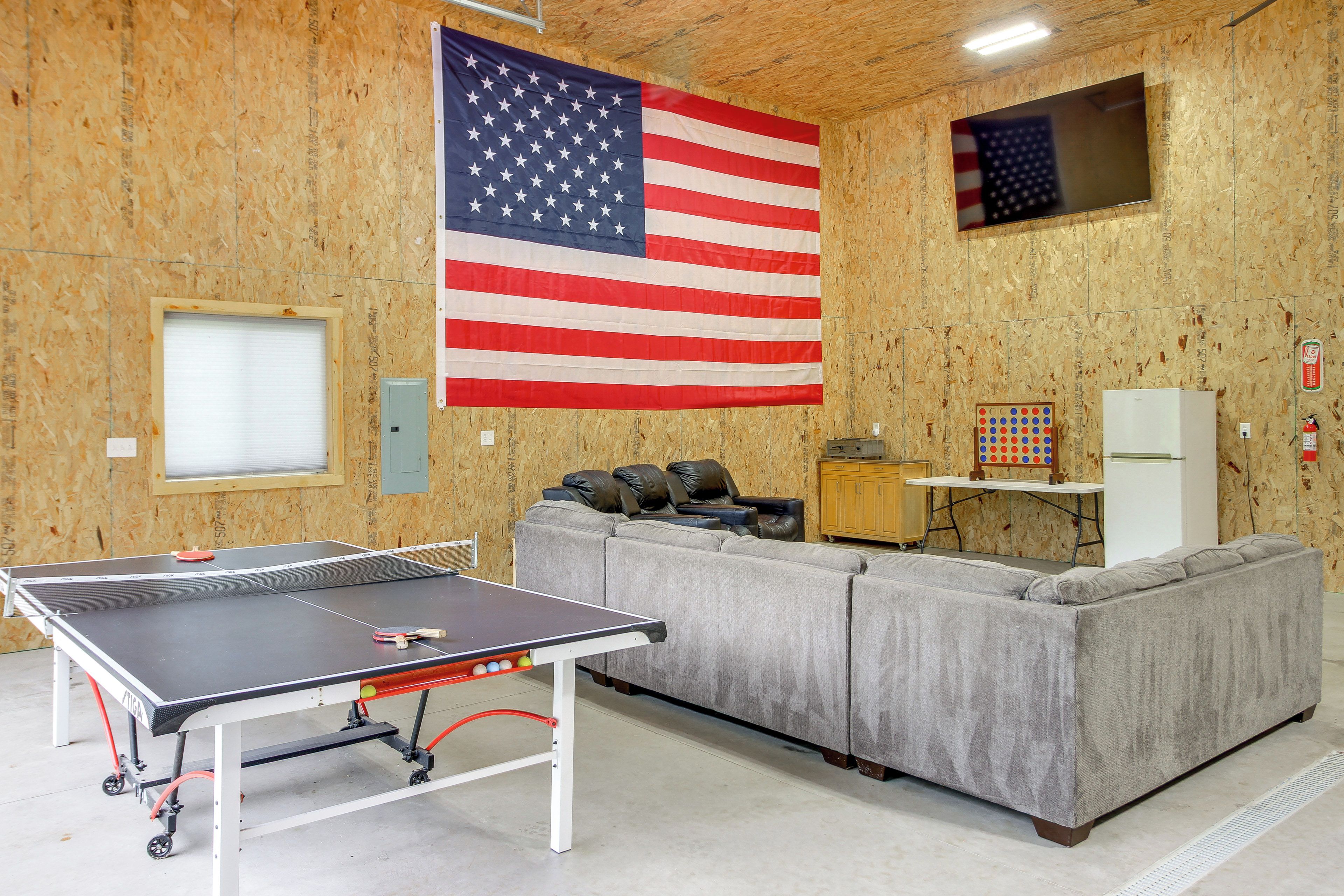 Una habitación con mesa de ping pong, sofá gris, televisor y bandera estadounidense.