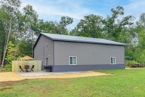 A single-story metal building with a flat roof, a fenced yard, and a patio with outdoor furniture. - 'Riverside Escape' Ride, Paddle, Relax (Crosby)