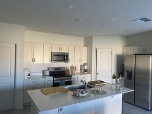 A modern kitchen with white cabinetry, stainless steel appliances, and a central island with a sink and stools.
