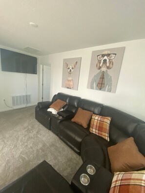 A living room with a black leather sofa, two brown pillows, a plaid pillow, and a black coffee table with two metallic bowls.
