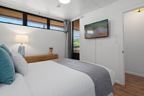Ein Schlafzimmer mit einem Bett, einem Nachttisch, einer Lampe, einem Fernseher und einem Fenster mit Vorhängen.