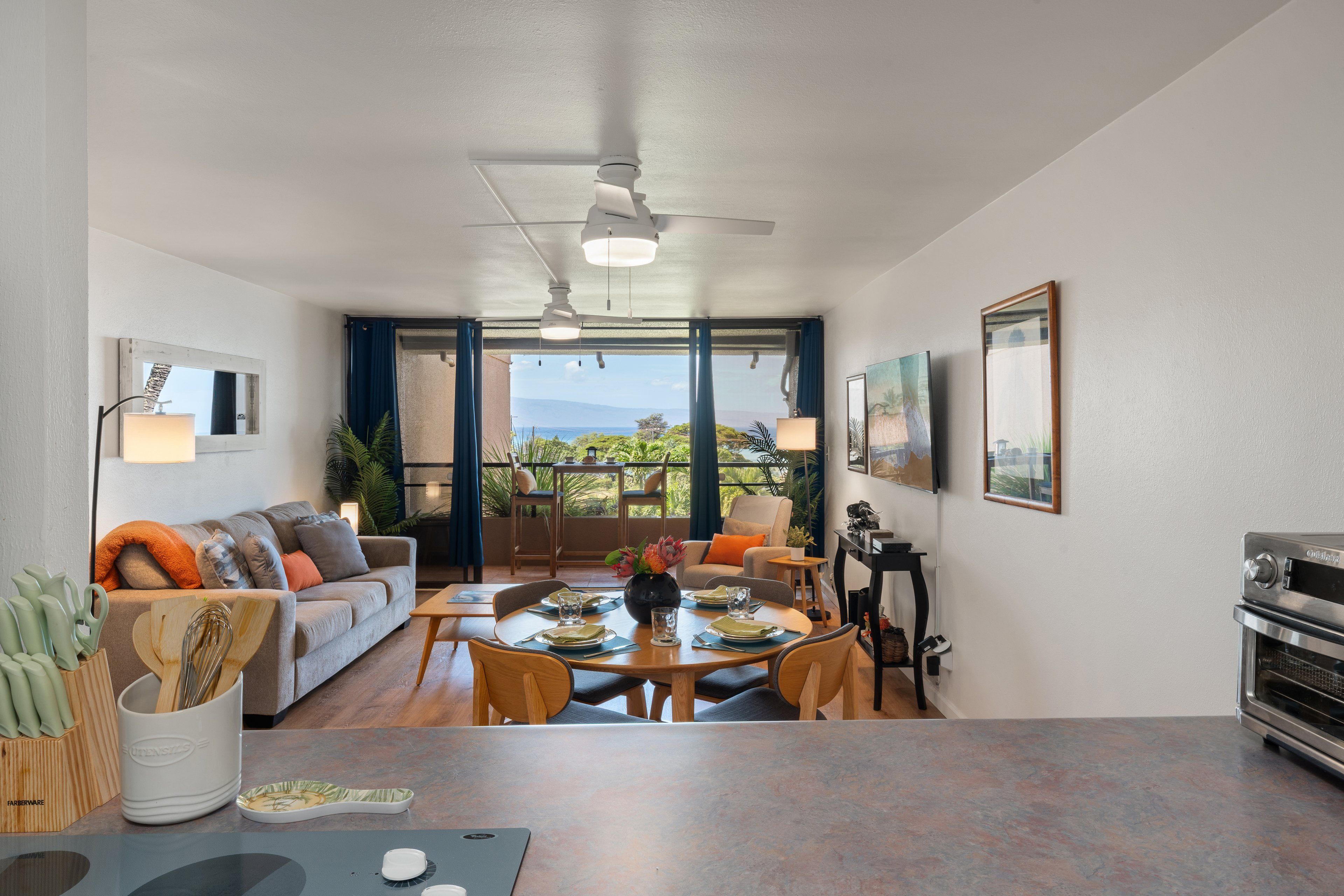 A modern living room with a dining area, a ceiling fan, and a view of the outdoors.