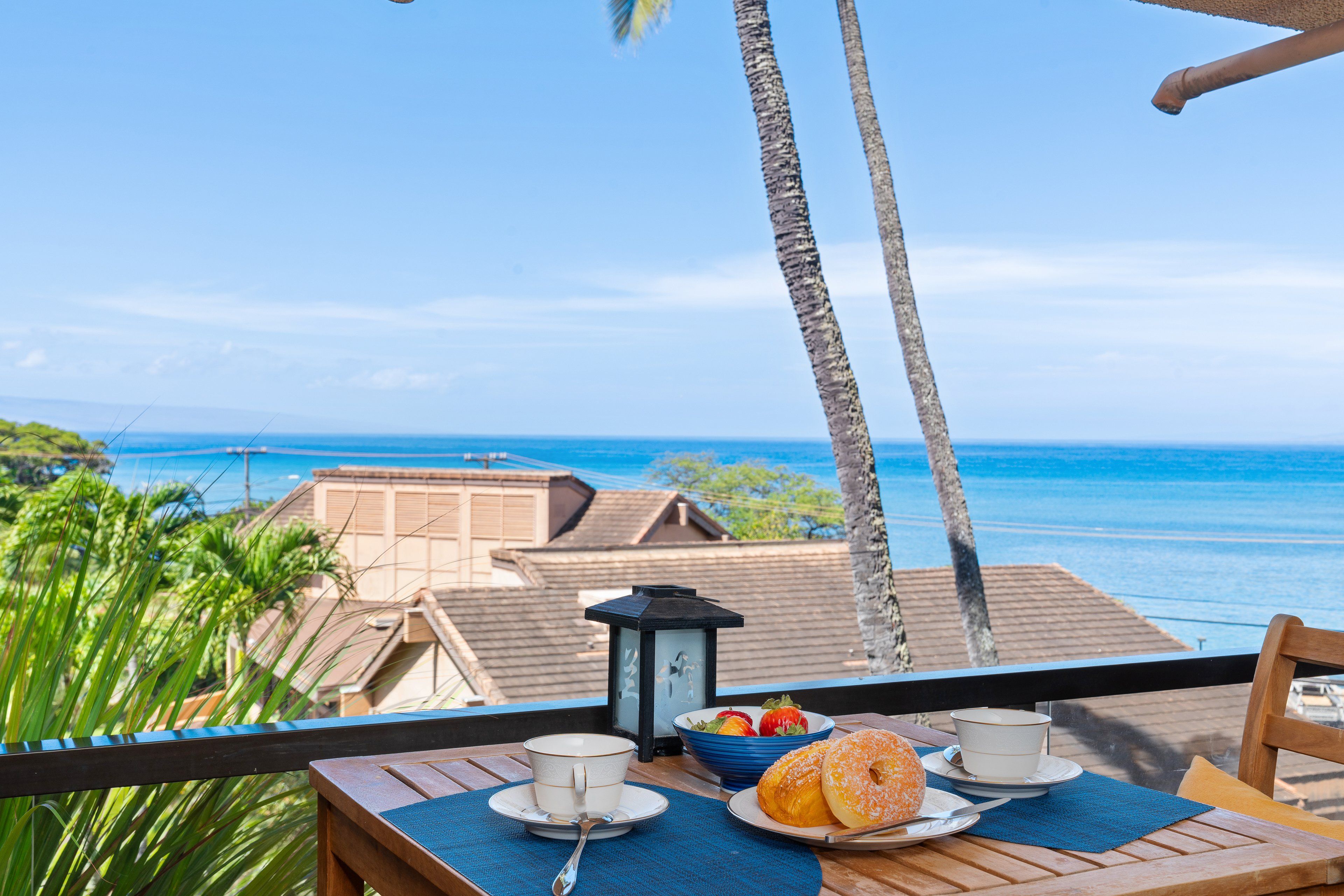 A table with a view of the ocean, a bowl of fruit, and a cup on a balcony.