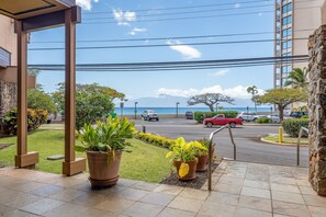 A hotel entrance with a view of the sea and mountains, outdoor plants, and a parking area with cars. - 1BD Condo with Ocean & Sunset Views Near Beach -Kahana Villas F407 (Lahaina)