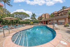 A swimming pool with lounge chairs and umbrellas, surrounded by palm trees and a building with balconies. - 1BD Condo with Ocean & Sunset Views Near Beach -Kahana Villas F407 (Lahaina)