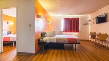 Quarto de hotel com cama, escrivaninha e televisão.