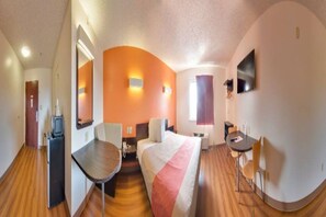 Ein Hotelzimmer mit Bett, Schreibtisch, Stuhl, Fernseher und Fenster.