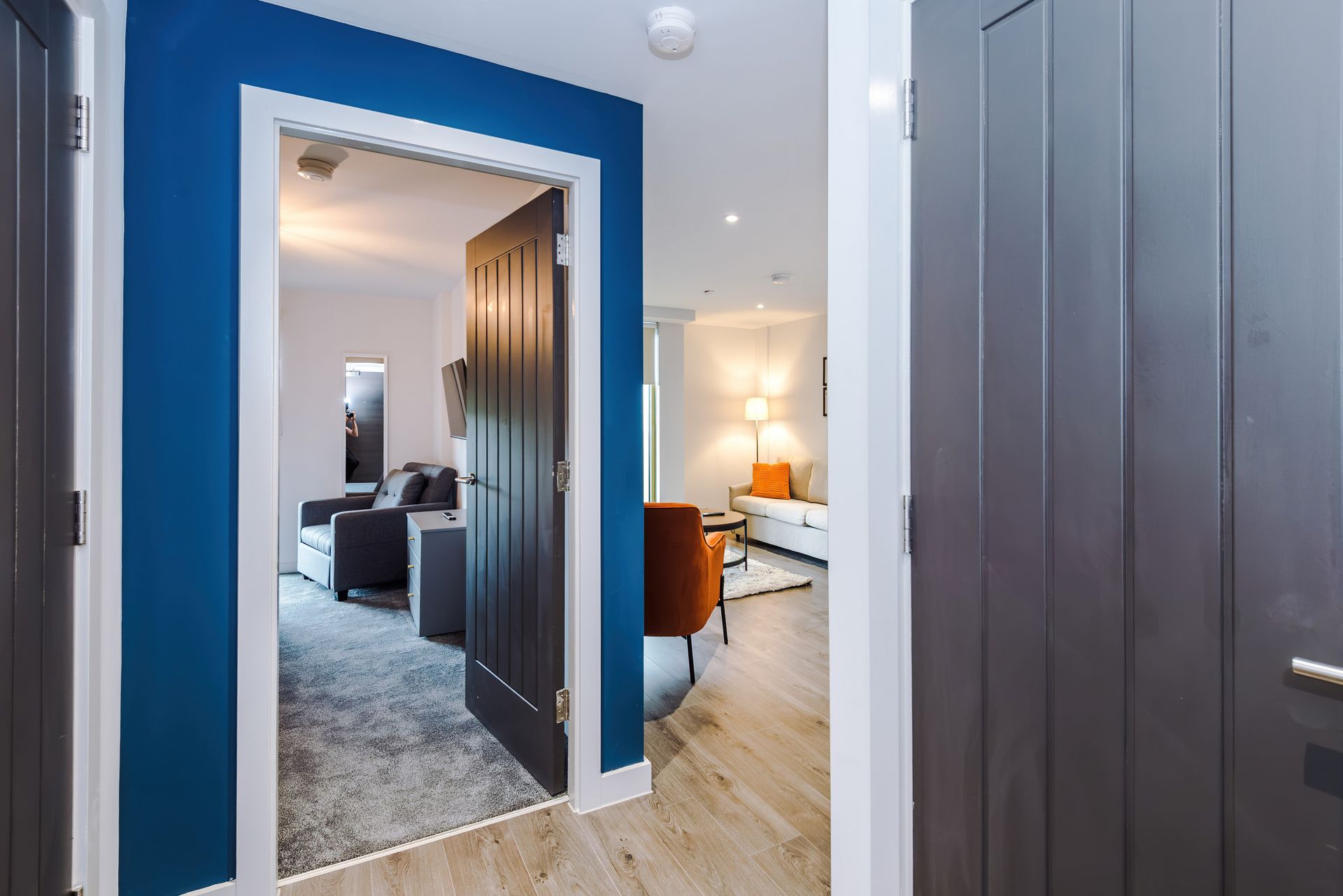 A hallway with a blue accent wall leading to a bedroom with a bed, a desk, and a chair.