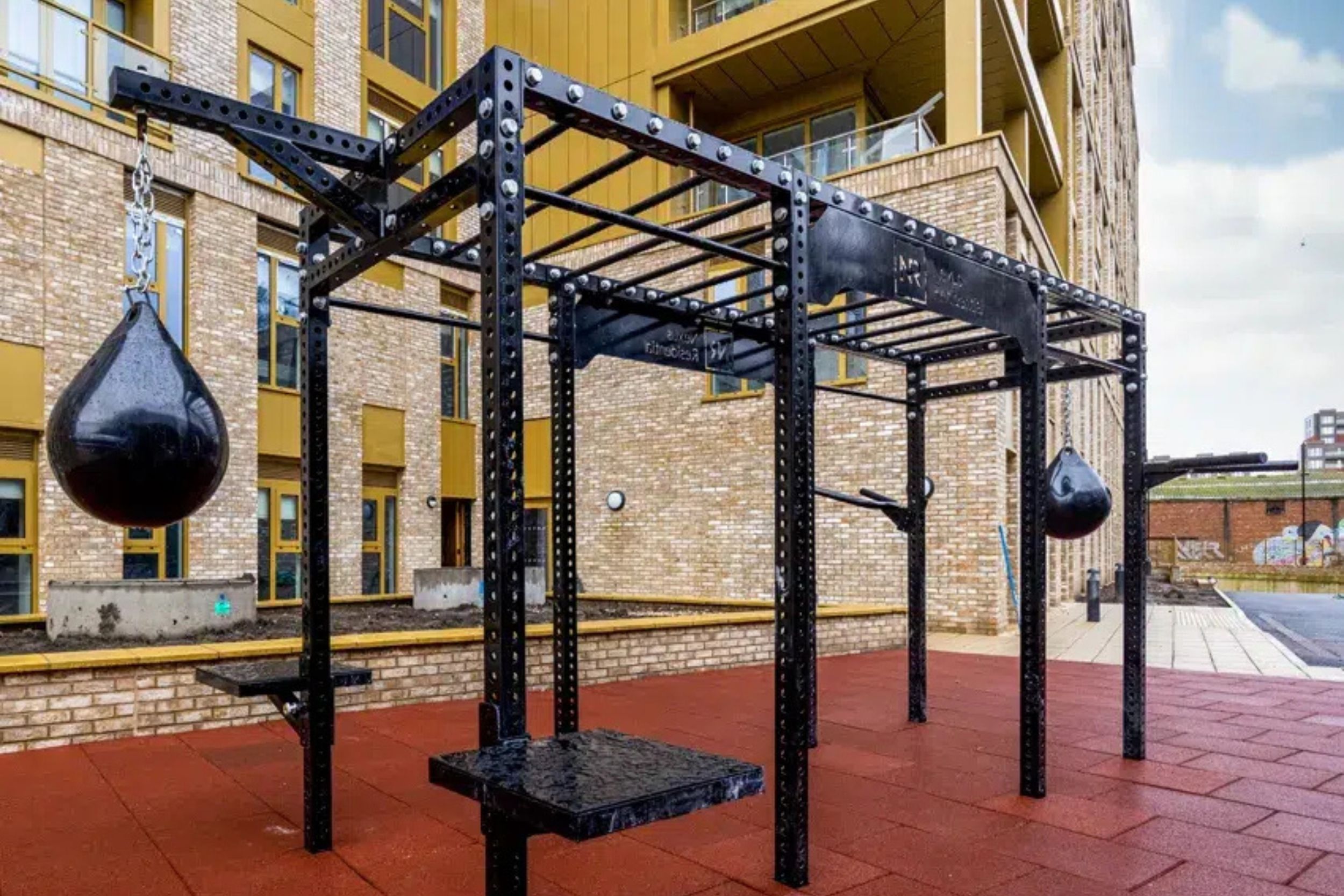 A metal outdoor gym structure with punching bags and a bench.