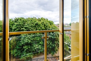 A view through a window with a yellow frame, overlooking a dense green tree canopy and a residential area. - Stylish and Cosy 1 BDR Apt in Liverpool (Liverpool)