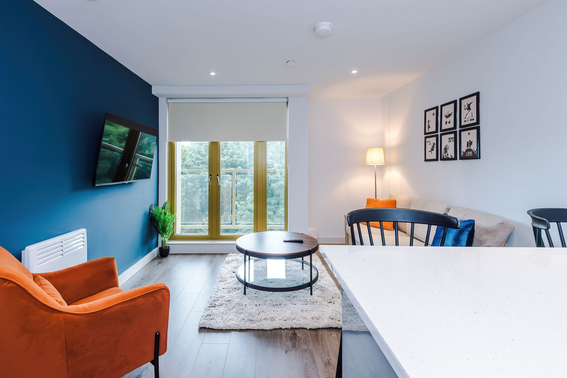 Una sala de estar moderna con un ventanal grande, un televisor de pantalla plana, una zona de comedor con mesa y sillas, y un sofá.