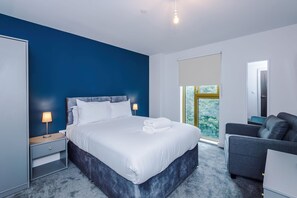 A modern hotel room with a large bed, a desk, a chair, and a window with a view of trees. - Stylish and Cosy 1 BDR Apt in Liverpool (Liverpool)