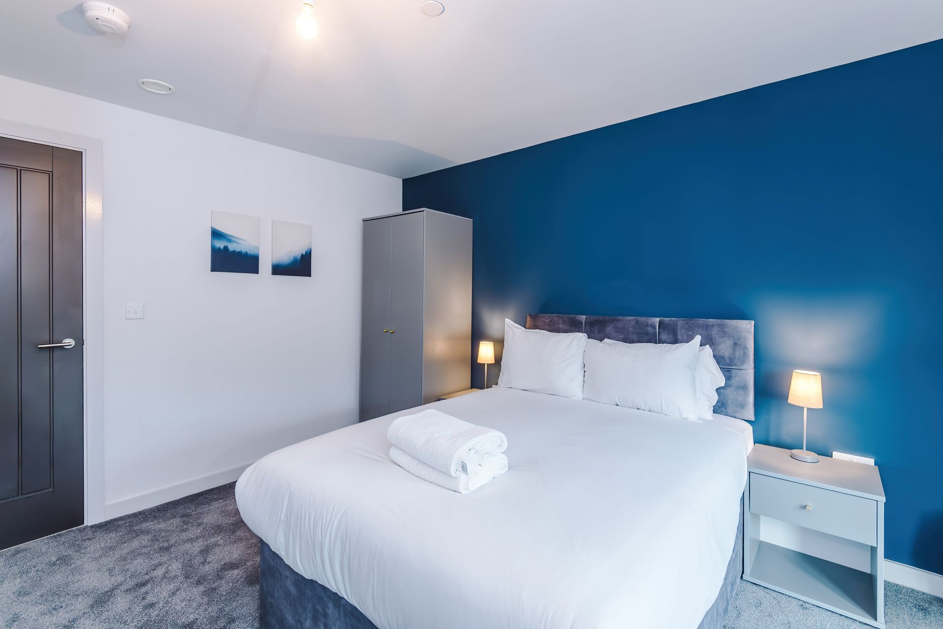 A hotel room with a bed, bedside tables, a wardrobe, and a door.