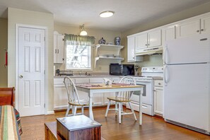 A compact kitchen with white cabinetry, a dining table, chairs, a microwave, an oven, and a refrigerator.
