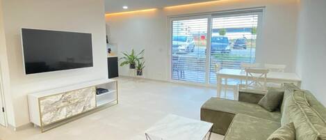 A modern living room with a flat-screen TV, a sofa, a coffee table, and a balcony with a view.