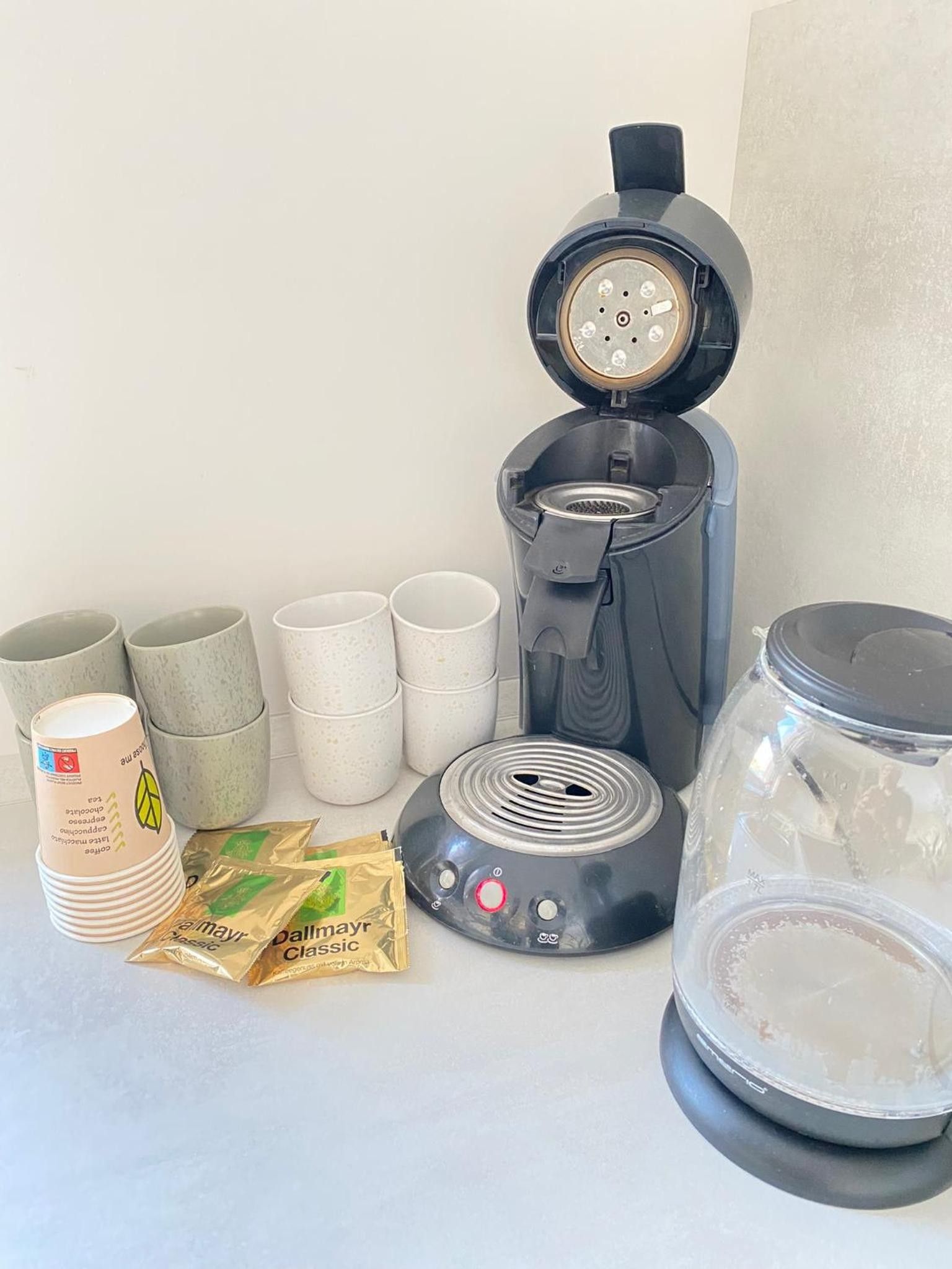 En kaffebryggare, engångsmuggar, en burk och kaffekapslar på ett bord.