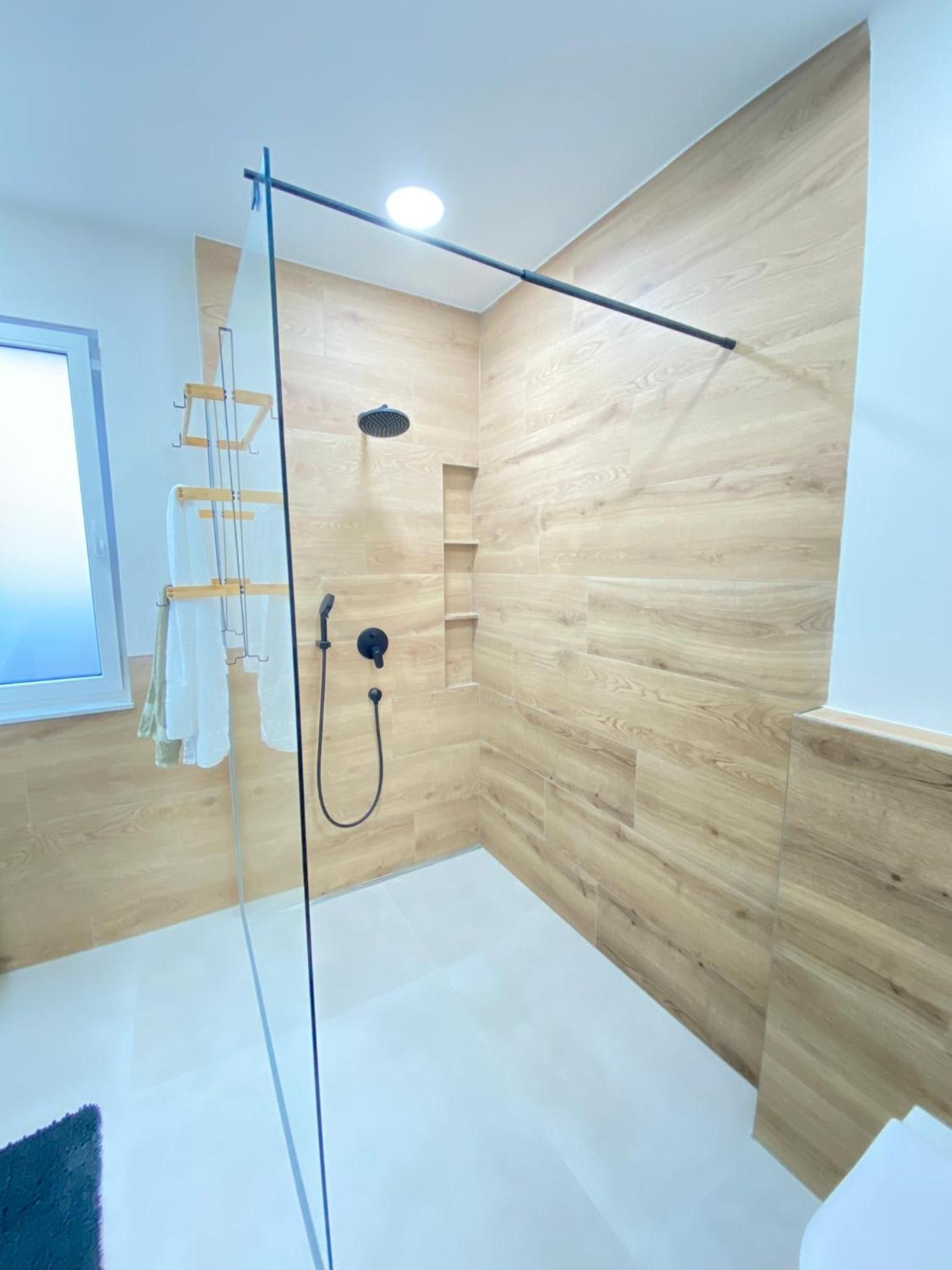 Ein modernes Badezimmer mit einer gläsernen Duschkabine, Holzpaneelen an den Wänden und einem Fenster.