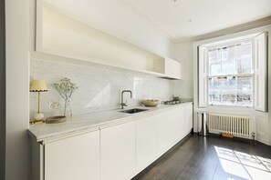 Eine moderne Küche mit weißen Schränken, einer Marmor-Spritzschutzwand, einem Spülbecken und einem Fenster mit schmiedeeisernen Gitterstäben.