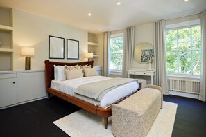 A bedroom with a bed, bedside tables, a mirror, and a view of greenery outside. - Notting Hill Floor by Floor (London)