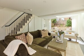 A modern living room with a staircase, a green sofa, a coffee table, and a view of the outside. - Notting Hill Floor by Floor (London)