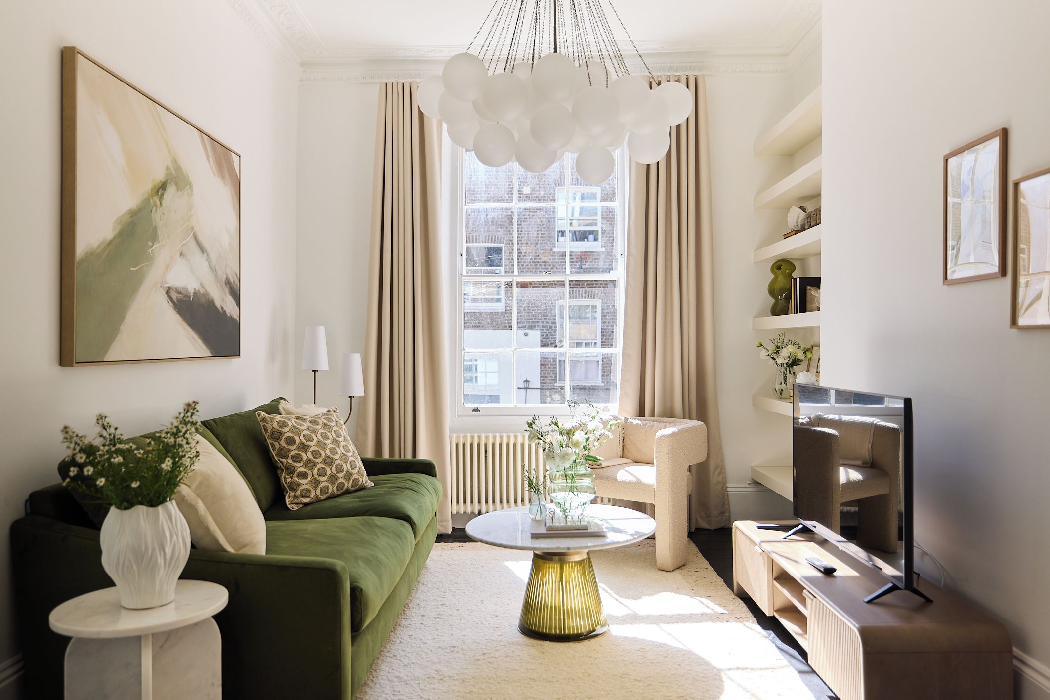 A modern living room with a green sofa, a round coffee table, a television, and a large window with curtains.
