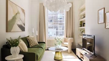 A modern living room with a green sofa, a round coffee table, a television, and a large window with curtains.