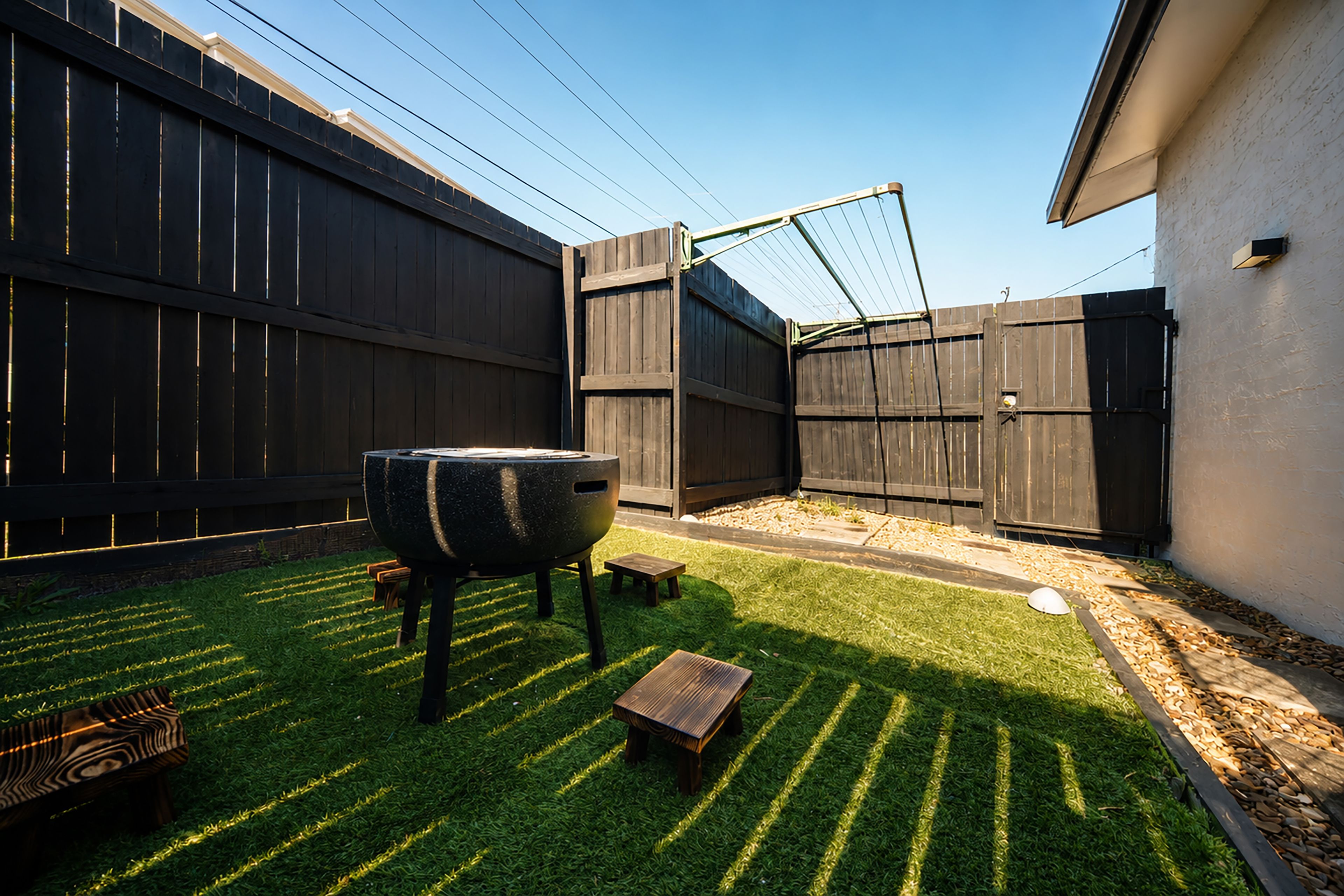 A backyard with a barbecue grill, a wooden bench, and a fenced area.