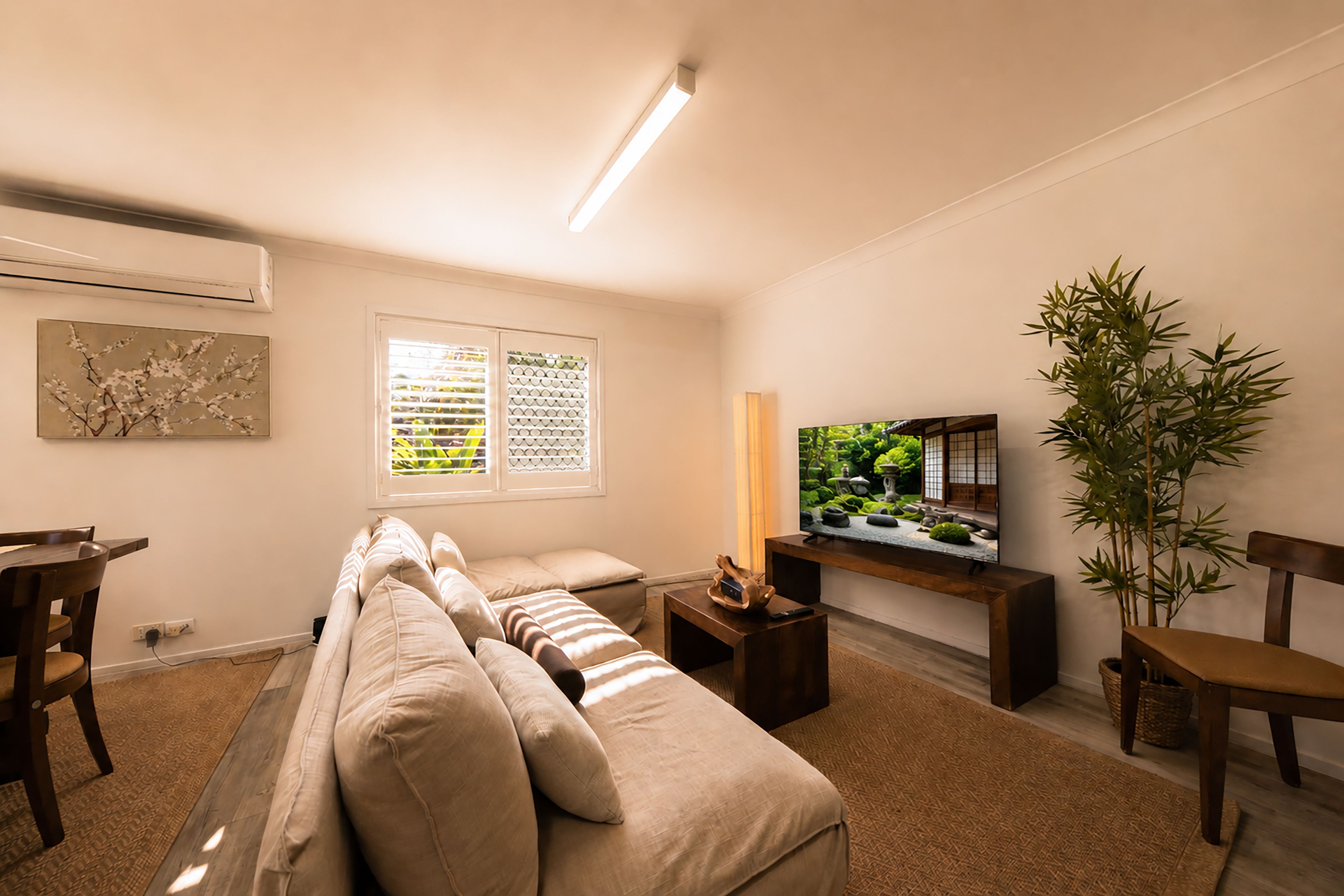 A living room with a sofa, a television, a plant, and a window with blinds.