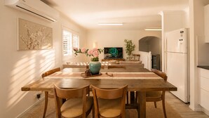 A modern kitchen with a dining area, featuring a wooden table, chairs, a TV, and a refrigerator. - Zen Retreat: Cinema, Pet-Friendly Yard (Springwood)