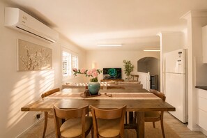 A modern kitchen with a dining area, featuring a wooden table, chairs, a TV, and a refrigerator. - Zen Retreat: Cinema, Pet-Friendly Yard (Springwood)