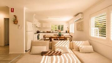 A modern living room with a sofa, a dining table, and a kitchen in the background.