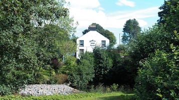 A white building with a sign reading 'Stanley Arms Hotel' surrounded by lush greenery and a stone pile.