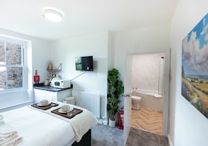A hotel room with a bed, a small kitchenette, a television, a bathroom, and a painting on the wall. - The Stanley Arms Hotel by Guestz (Seascale)