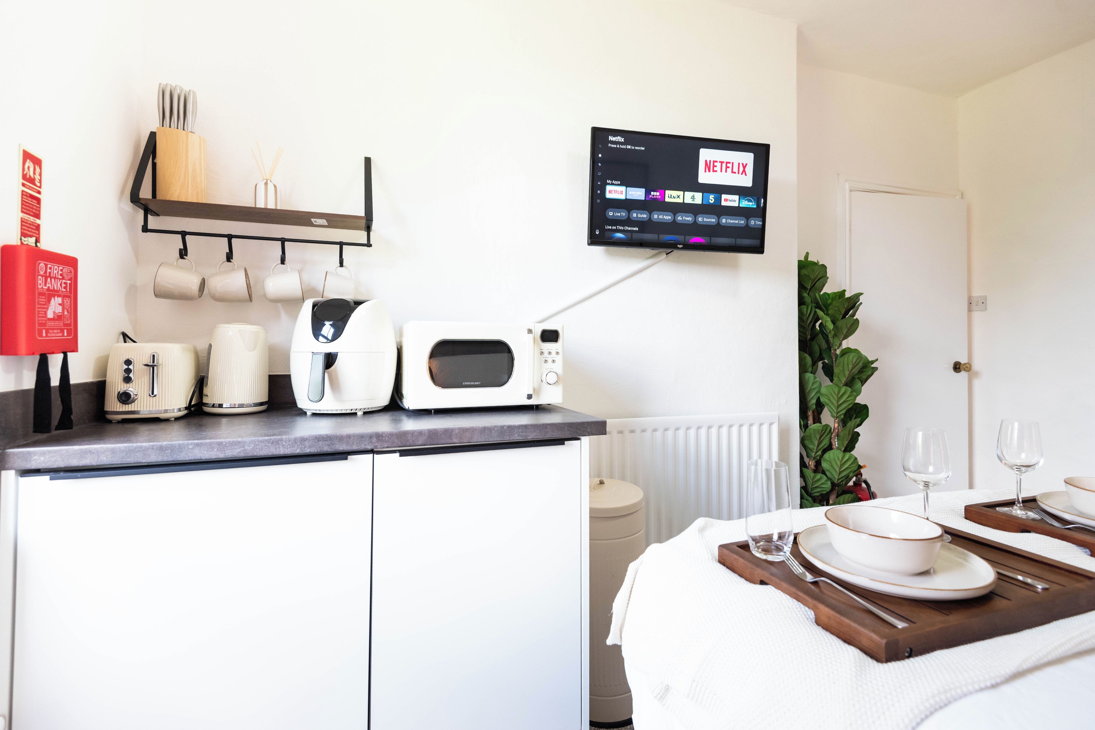 A kitchenette with a microwave, toaster, and coffee maker, a fire blanket, and a TV displaying Netflix.