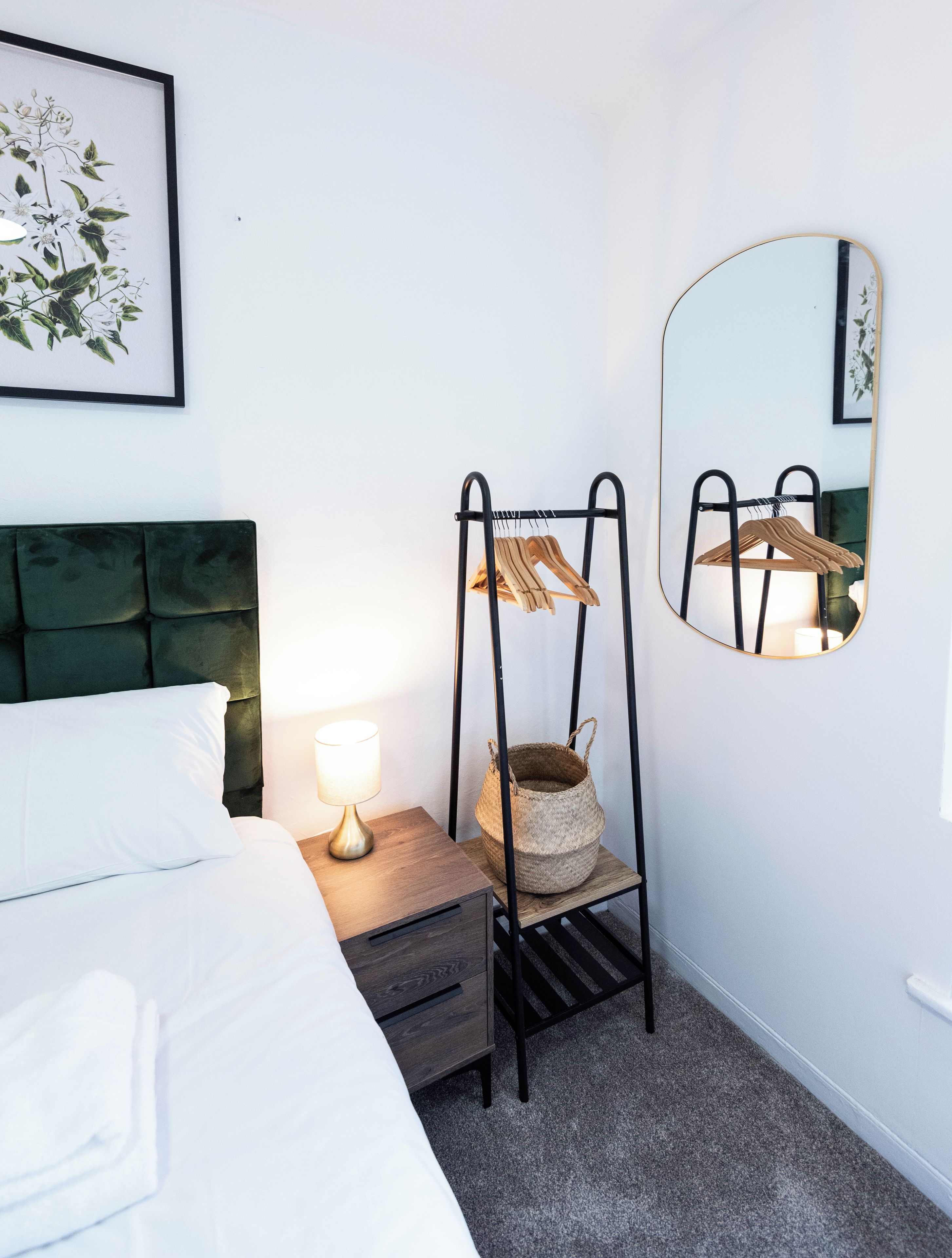 A neatly arranged bedroom with a bed, bedside table, lamp, and a wall-mounted mirror.