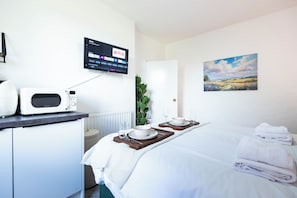 A hotel room with a bed, a bedside table with a microwave, a TV displaying Netflix, and a painting on the wall.