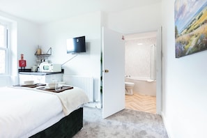 A hotel room with a bed, bedside table, a flat-screen TV mounted on the wall, a small kitchenette, and a bathroom with a toilet and shower. - The Stanley Arms Hotel by Guestz (Seascale)